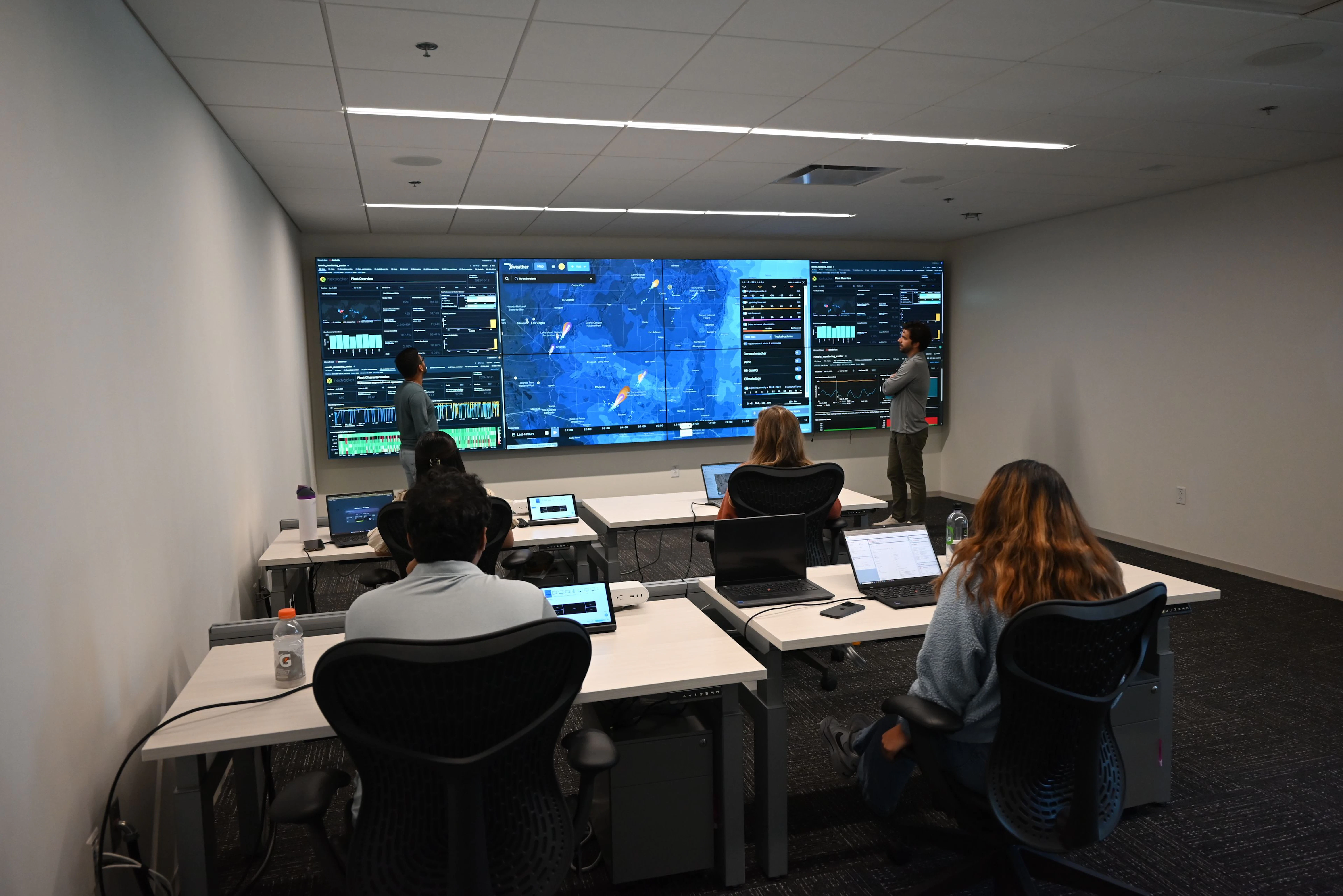 An operations room with a wall of hazard maps and dashboards